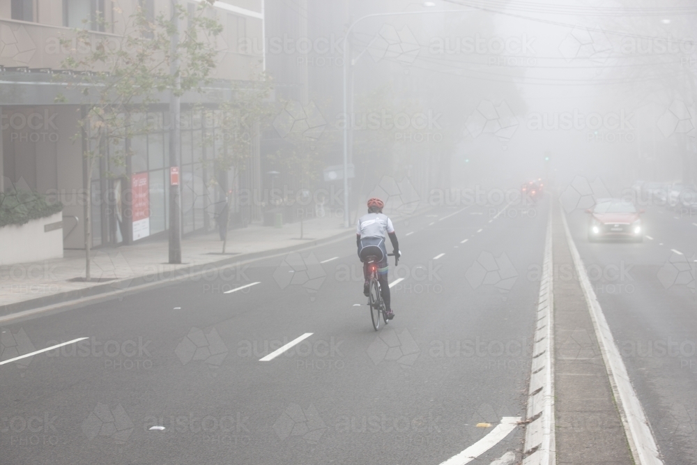 Cyclist riding down road in fog - Australian Stock Image