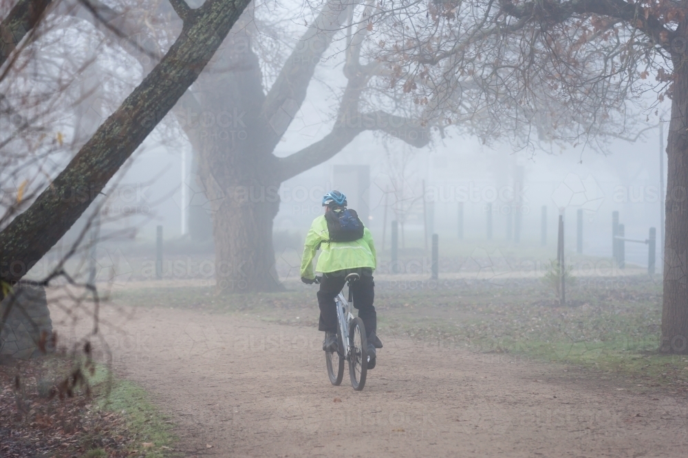 cyclist riding on a path through early morning fog - Australian Stock Image