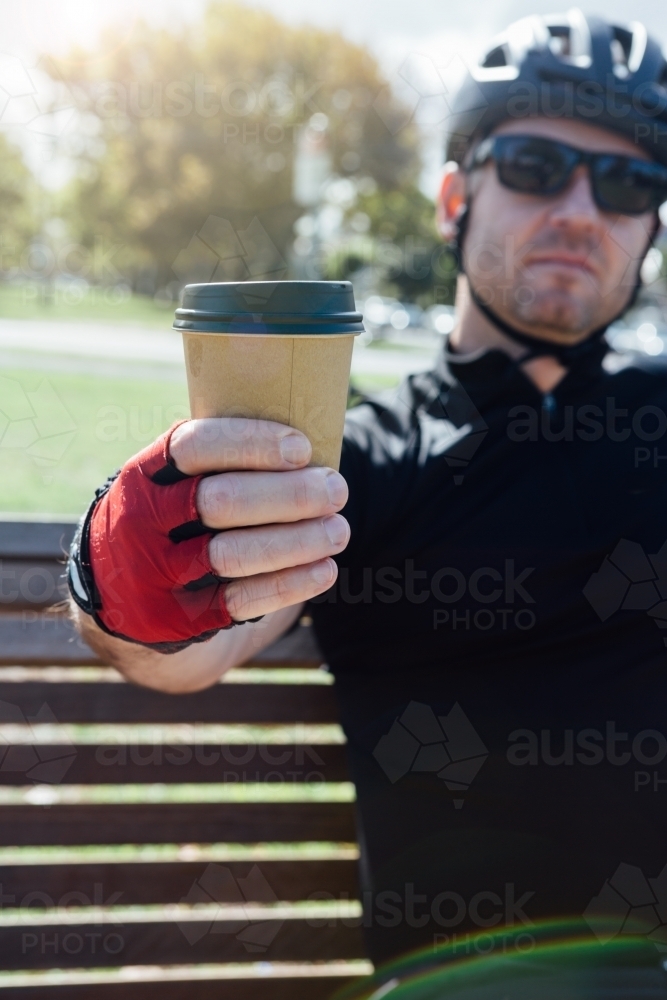 Cyclist taking a break holding a coffee to camera - Australian Stock Image