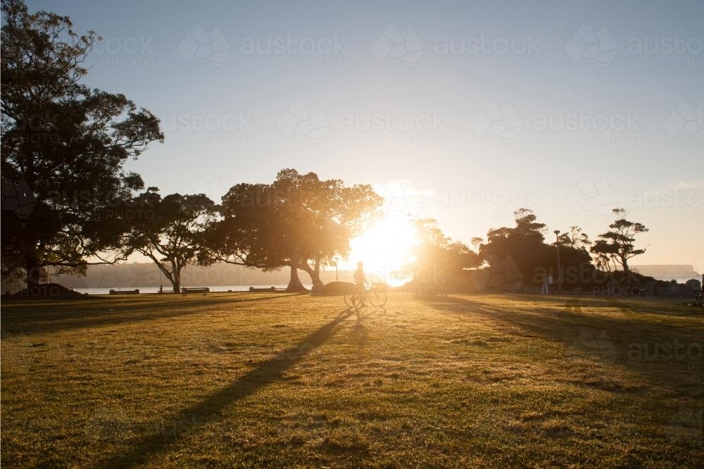 Cyclist walking bike across the sunrise at a park - Australian Stock Image