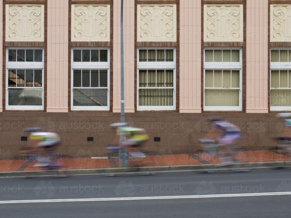 Cyclists racing on a road past an office building - Australian Stock Image
