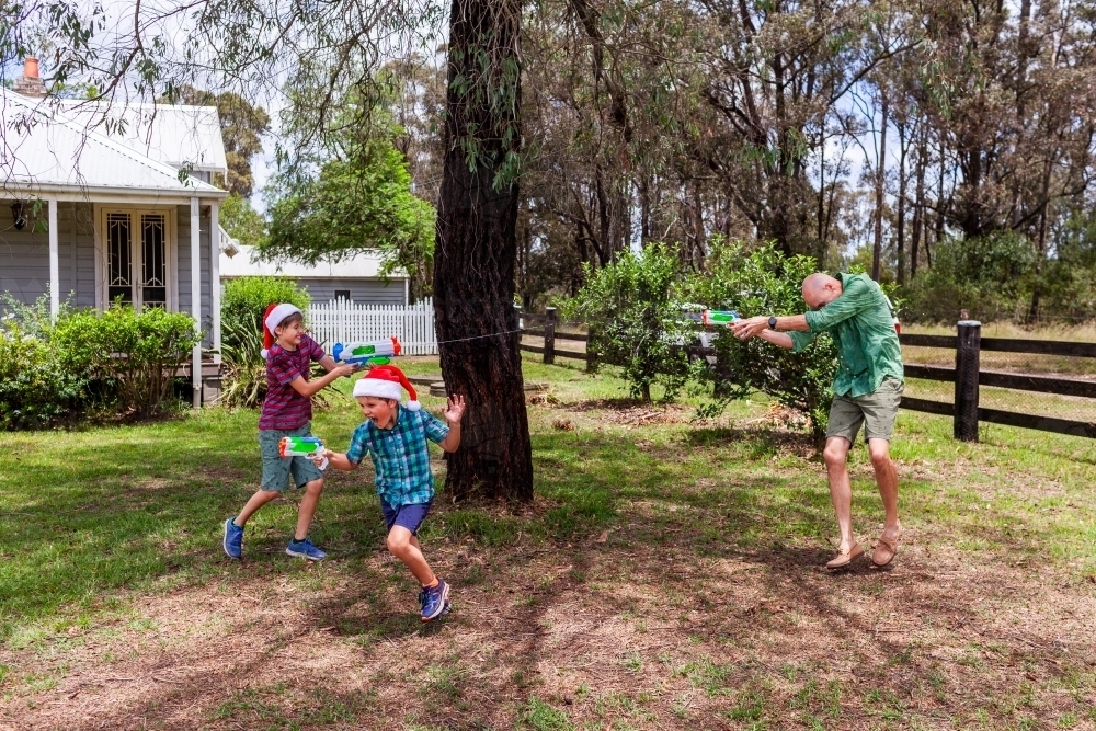 Dad and boys having water fight in front yard at Christmas - Australian Stock Image