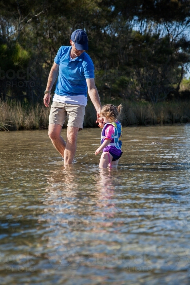 Image of Dad and child wade in shallow water where the river meets the