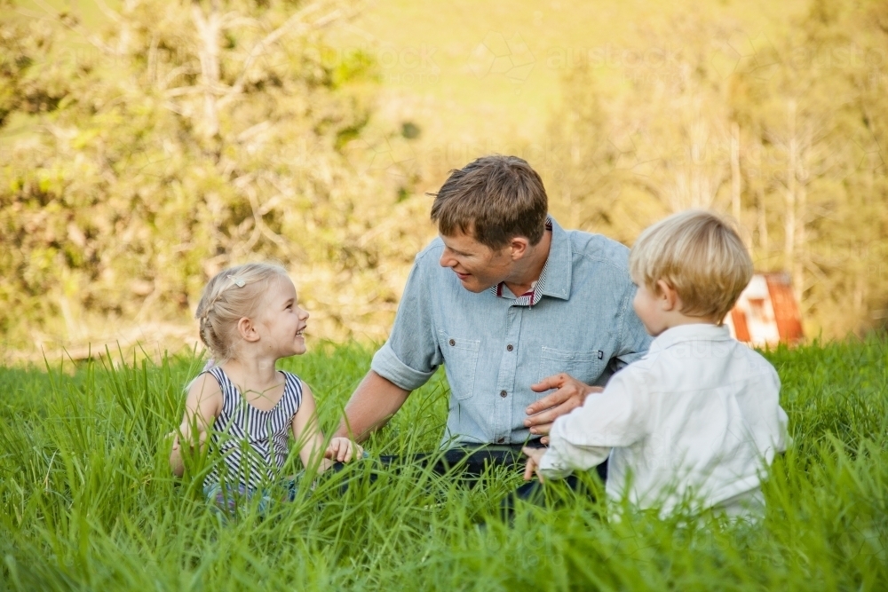 Dad and children sitting together in the grass - Australian Stock Image