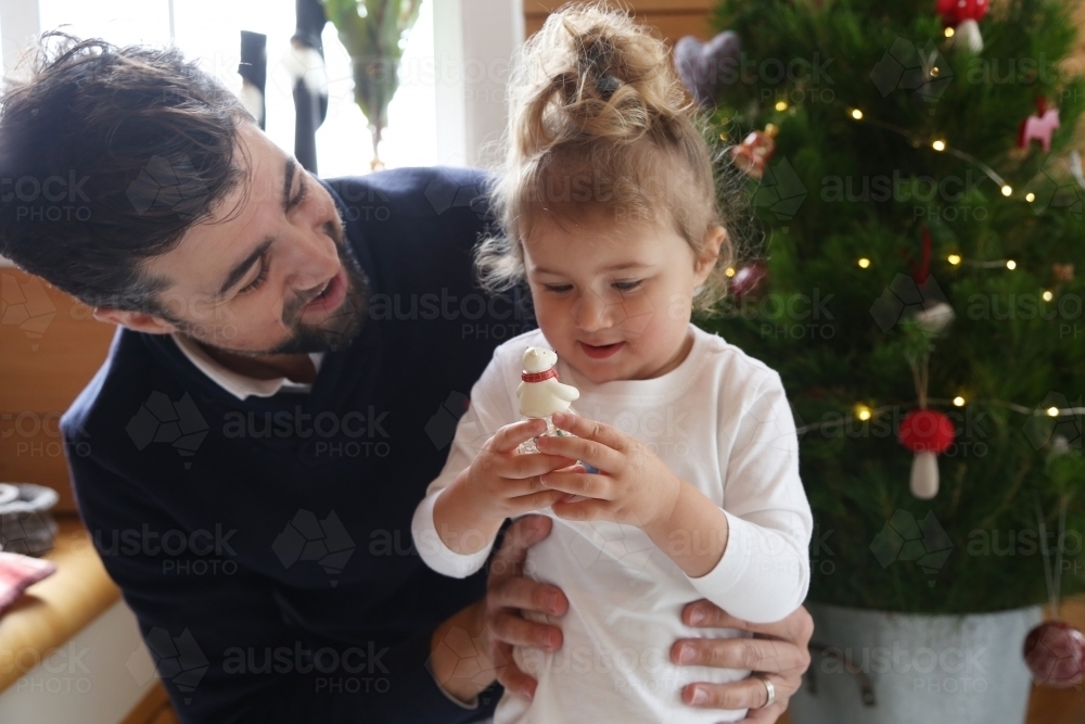 Dad and daughter looking at ornament with Christmas tree in background - Australian Stock Image