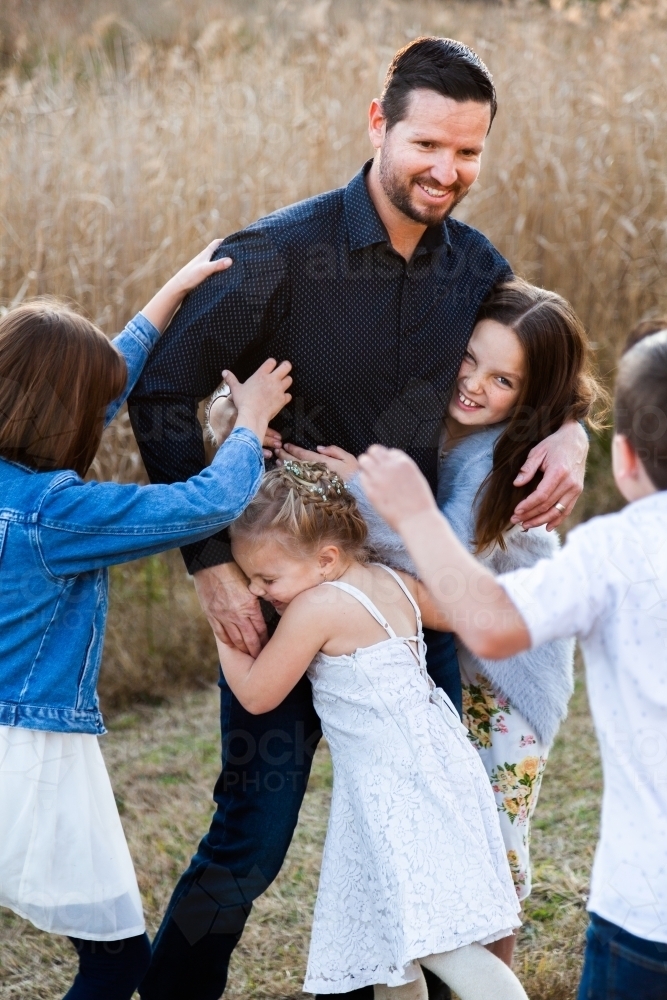 Dad being tackled by his children, having fun together outside - Australian Stock Image