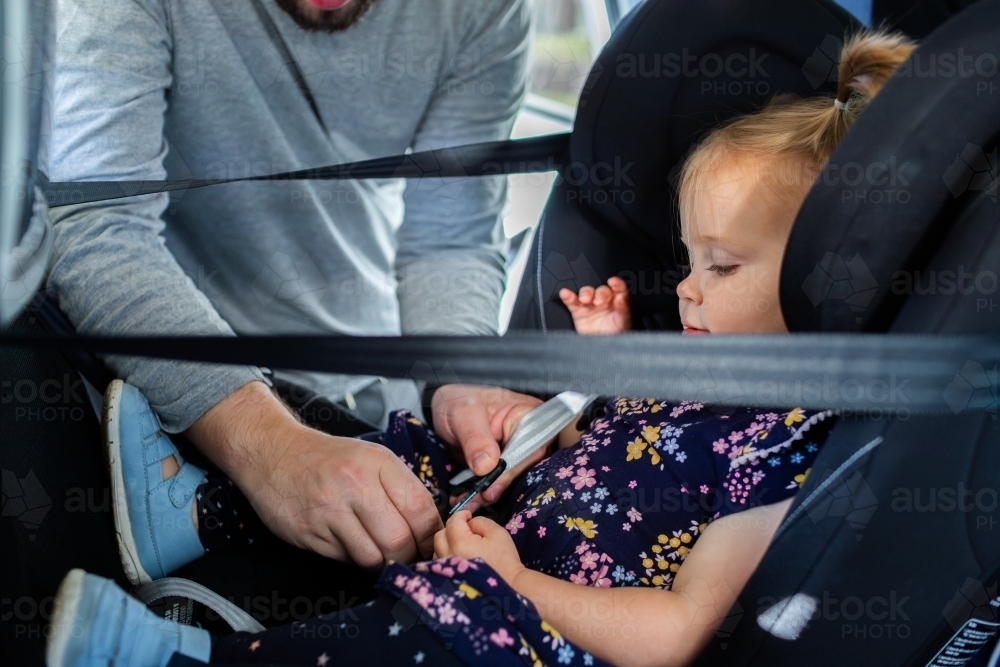 Dad buckling toddler into extended rear facing car seat - Australian Stock Image
