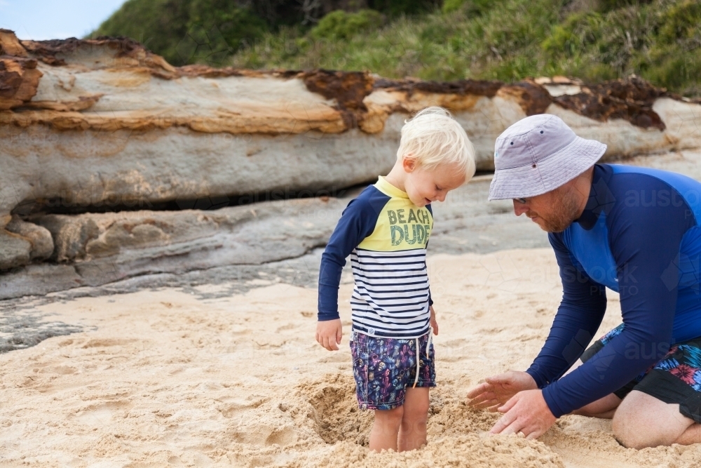 Dad burying boys feet in sand at the seaside - Australian Stock Image