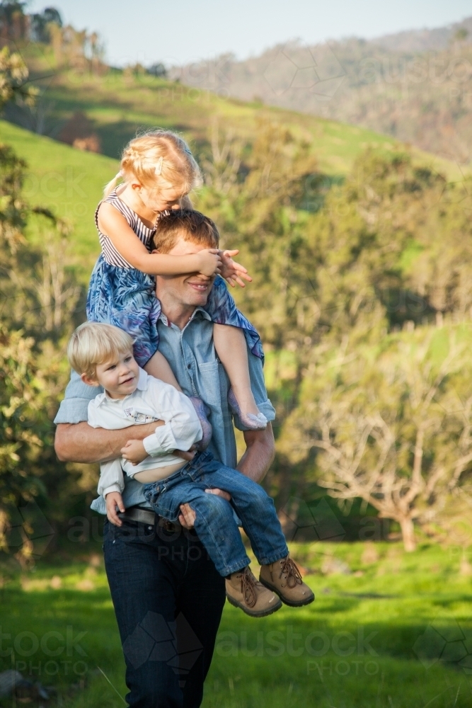 Dad carrying son and giving daughter a piggyback - Australian Stock Image