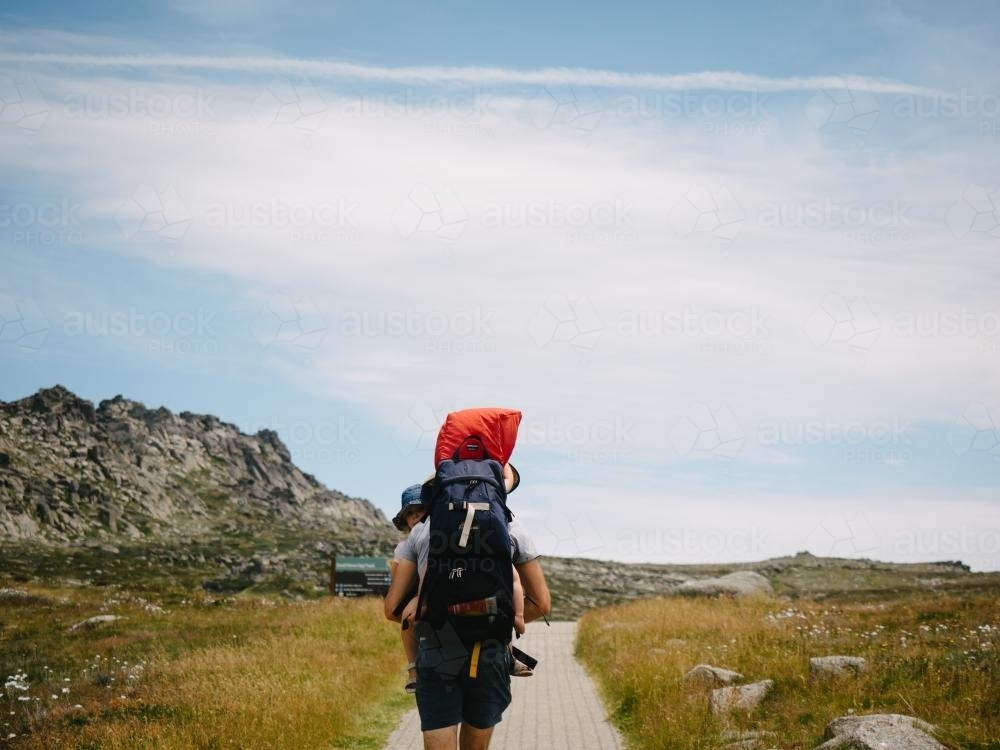 Dad carrying two kids walking along path in the mountains - Australian Stock Image