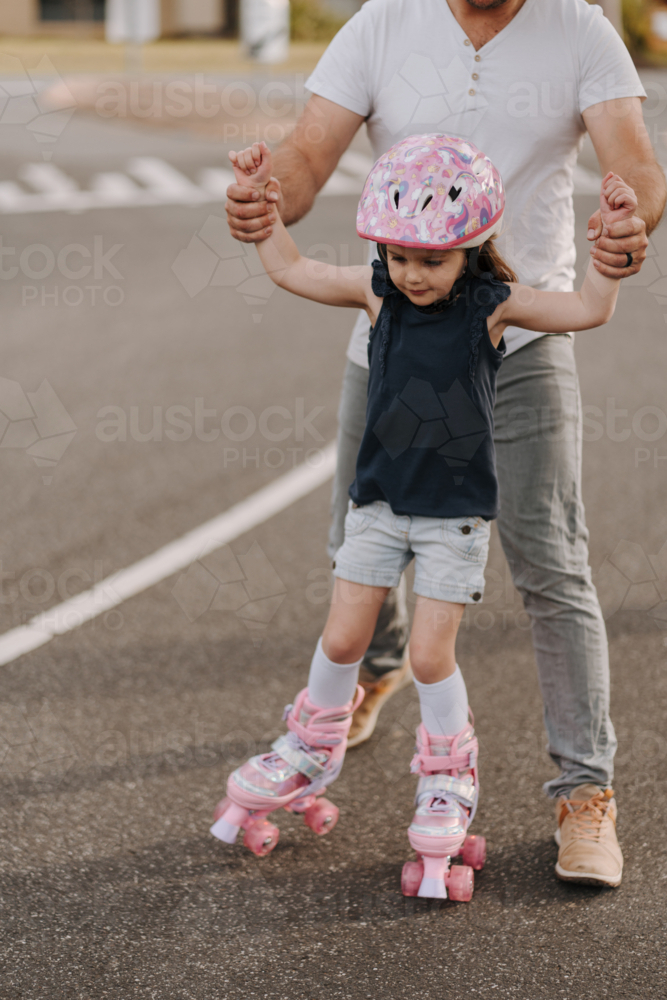 Dad helping daughter find balance in roller skates - Australian Stock Image