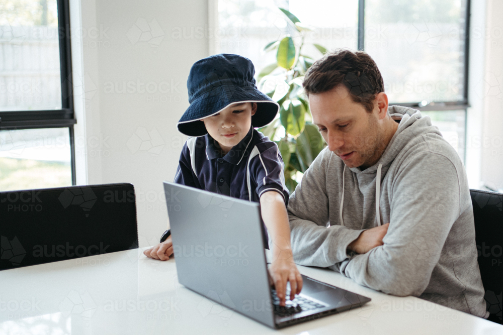 Dad helping kids with their homework using laptop - Australian Stock Image