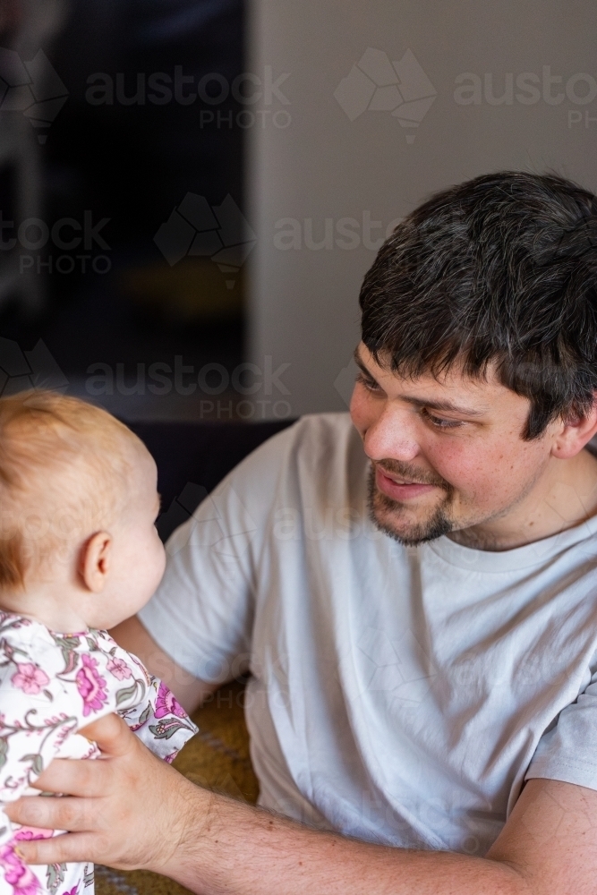 dad holding baby girl inside smiling together - Australian Stock Image