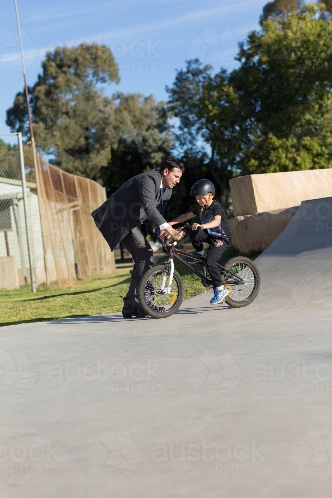 Dad in suit helping son on bike - Australian Stock Image