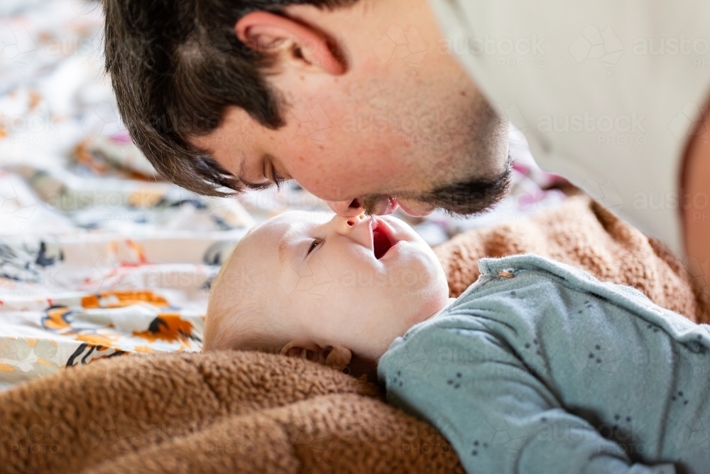 dad laughing with baby girl on bed sharing intimate moment together - Australian Stock Image