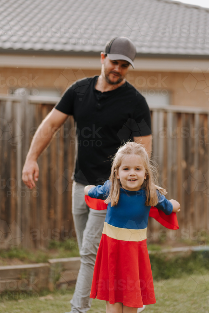 Dad playing with daughter in superhero costume in their yard. - Australian Stock Image