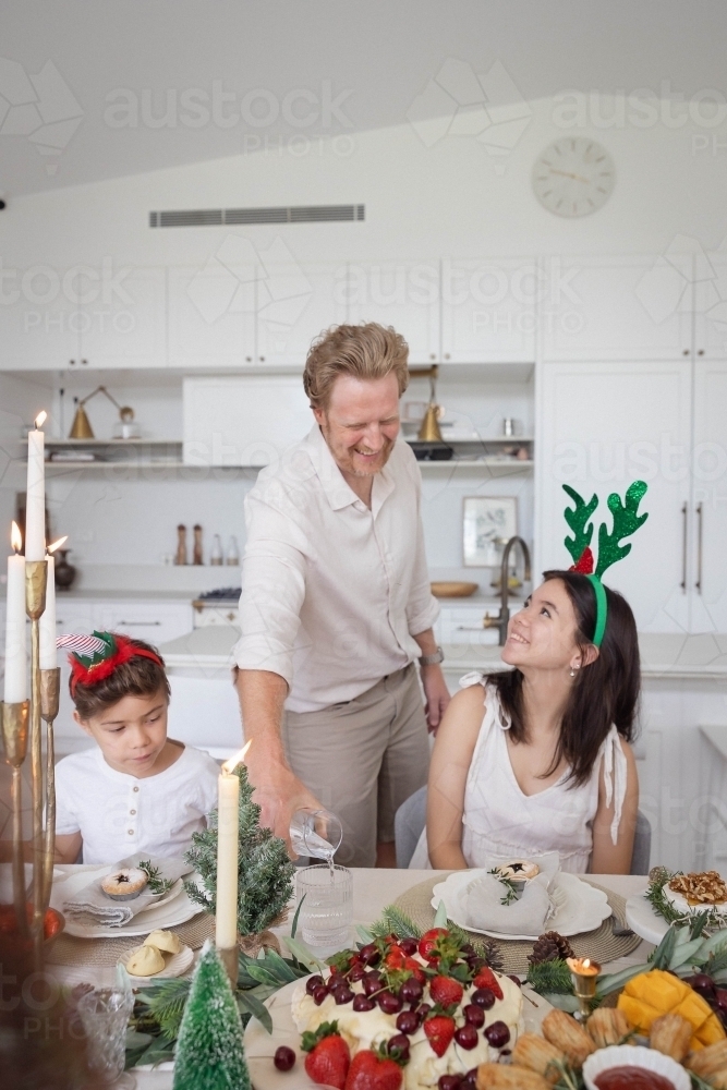 Dad pouring water for daughter and son at Christmas table - Australian Stock Image