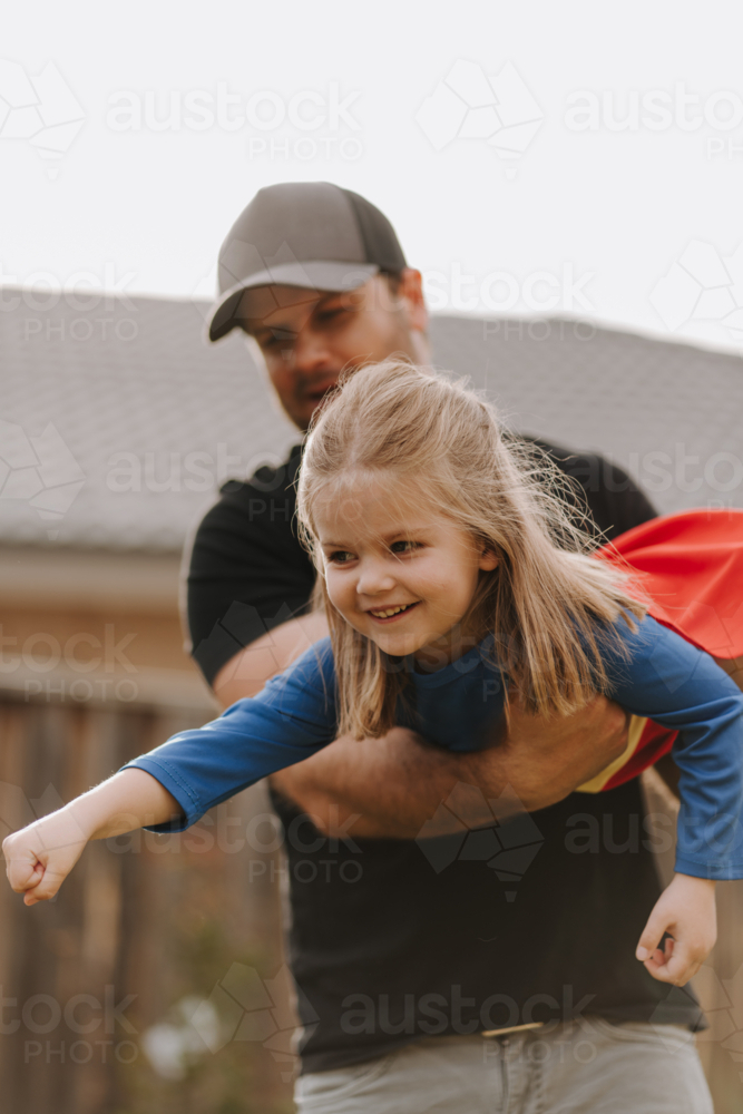 Dad simulating a flight for daughter in superhero costume. - Australian Stock Image