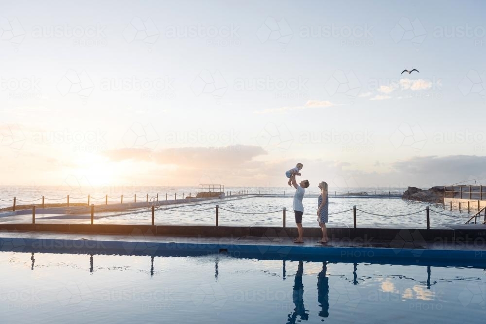 Dad throwing child in the air at sunrise over the ocean pool - Australian Stock Image