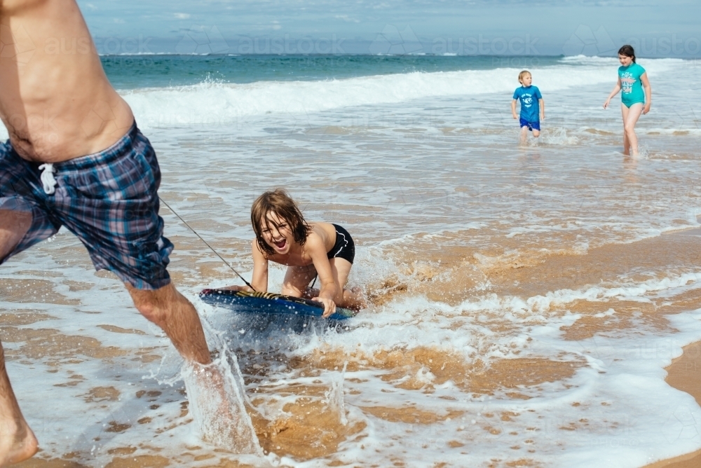 Dad tows boy on boogie board - Australian Stock Image