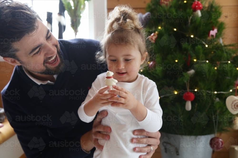 Dad with daughter looking at ornament with Christmas in background - Australian Stock Image