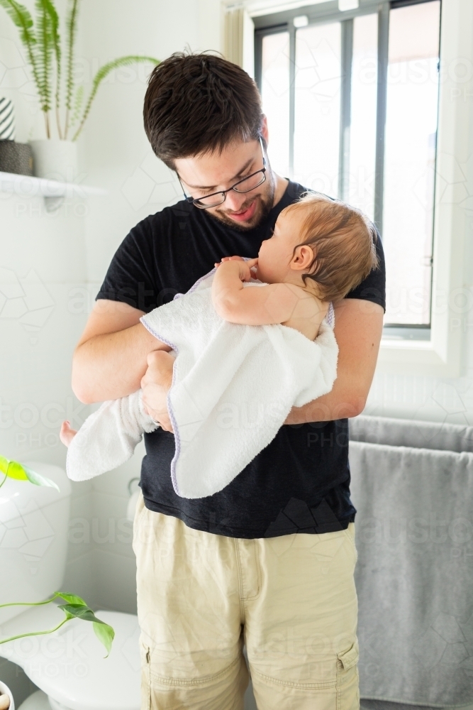 Daddy with baby drying off in towel after bath in bathroom - Australian Stock Image