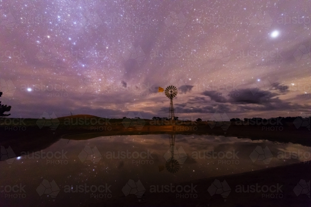 Dam with windmill at night under starry sky - Australian Stock Image