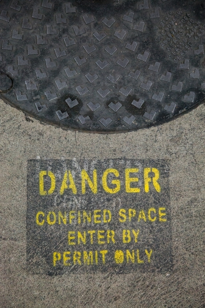 Danger confined space enter by permit only sign in car park beside man hole - Australian Stock Image