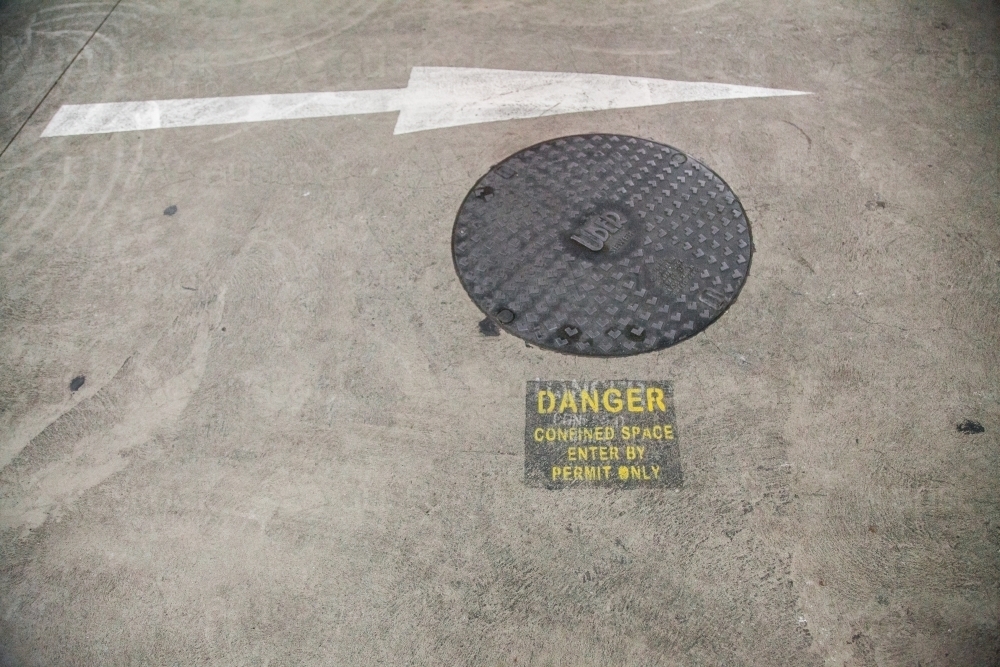 Danger confined space enter by permit only sign in car park beside man hole - Australian Stock Image