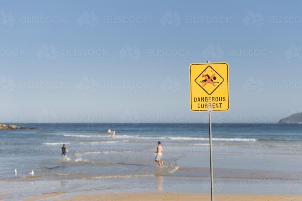 Dangerous Current Sign on the Beach with People Running In the Shallow Water - Australian Stock Image