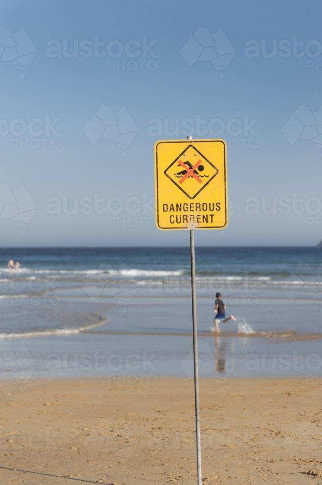 Dangerous Current Warning Sign on the Beach with Child Running In the Shallow Water - Australian Stock Image