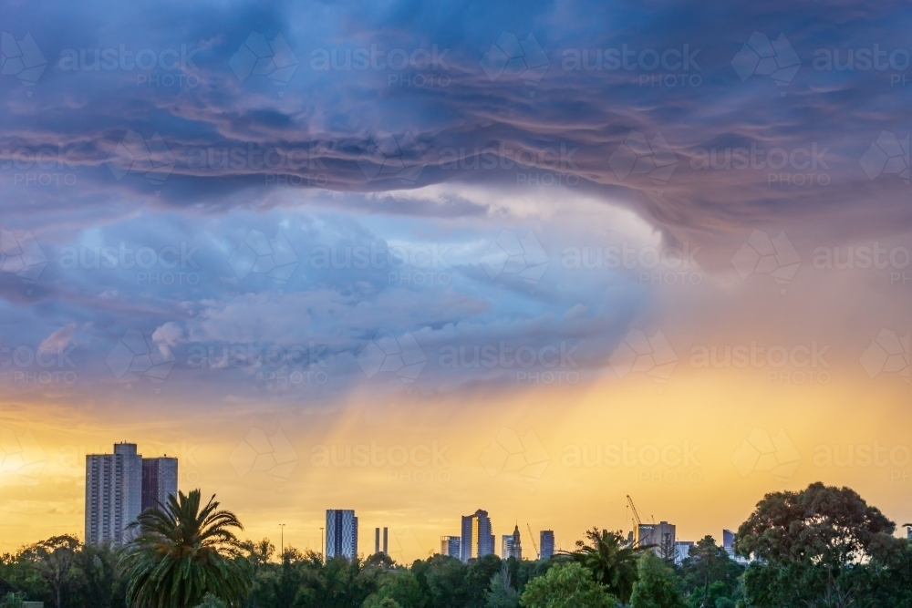 Dark cloud formations over a city skyline at sunset - Australian Stock Image
