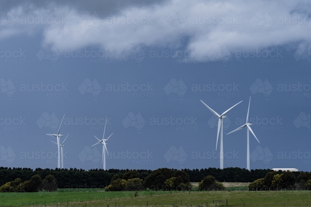 Dark stormy skies hovering over tall wind turbines - Australian Stock Image