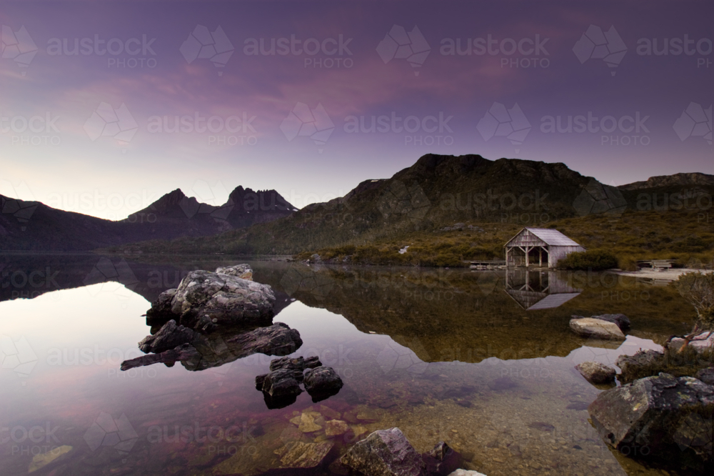 Dawn light reflects across the still waters of Dove Lake beneath Cradle Mountain - Australian Stock Image