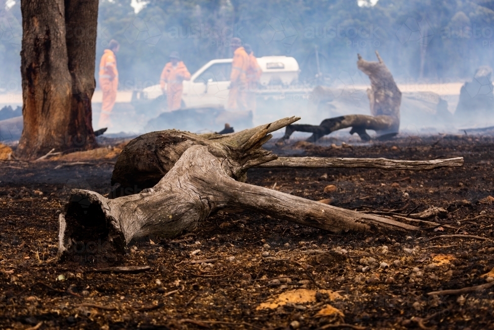 debris on foreground after a fire has been extinguished with firefighters in background - Australian Stock Image