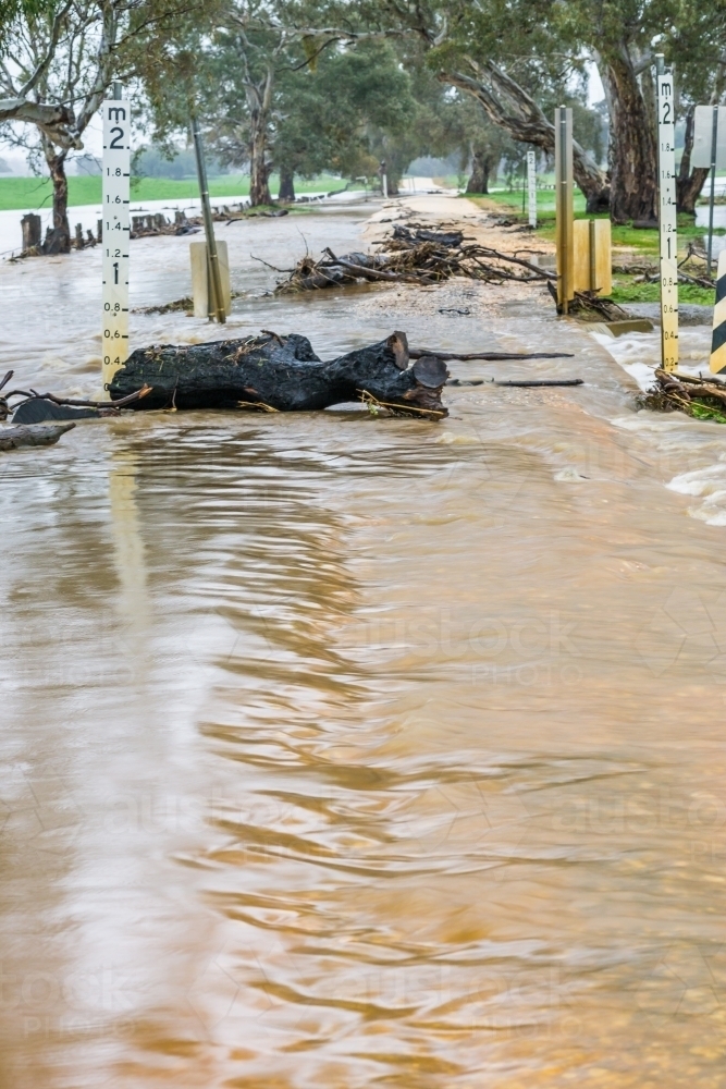 Debris sitting in flood waters rushing over a country road - Australian Stock Image