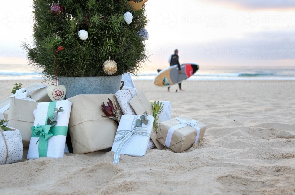Decorated Christmas tree with presents at beach with surfer in background - Australian Stock Image