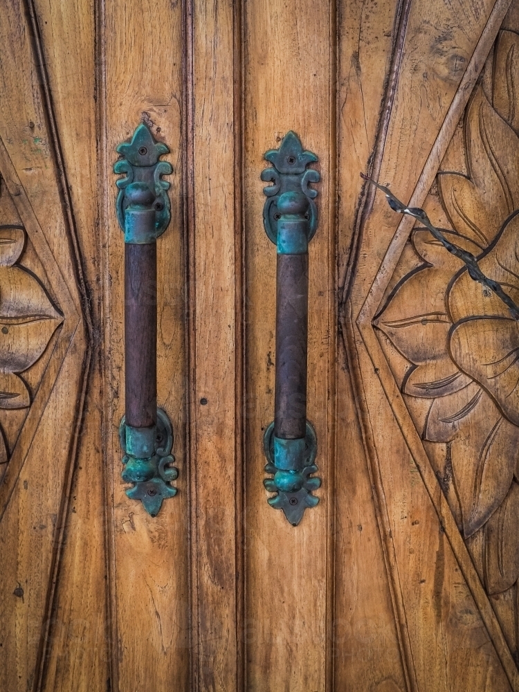 Decorative brass antique door handles on carved wooden door - Australian Stock Image