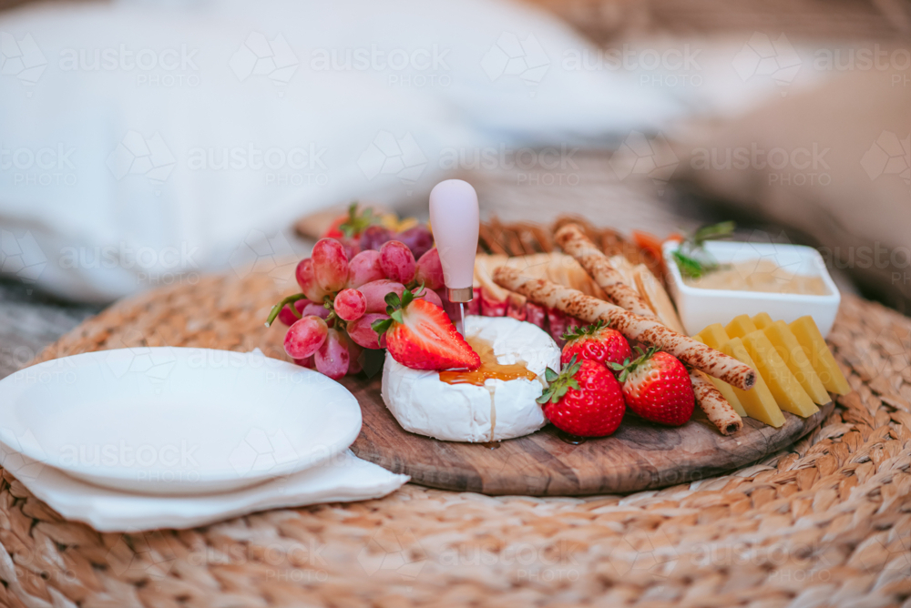 Delicious cheese platter featuring fresh fruits and snacks for a casual outdoor gathering - Australian Stock Image