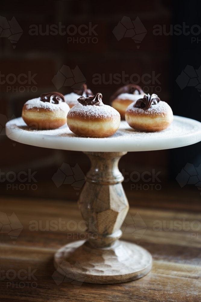 Delicious chocolate topped donuts on a vintage cake stand in a restaurant - Australian Stock Image