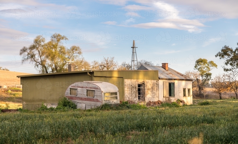 Derelict farm house with caravan out the back in the dappled sun lit evening - Australian Stock Image