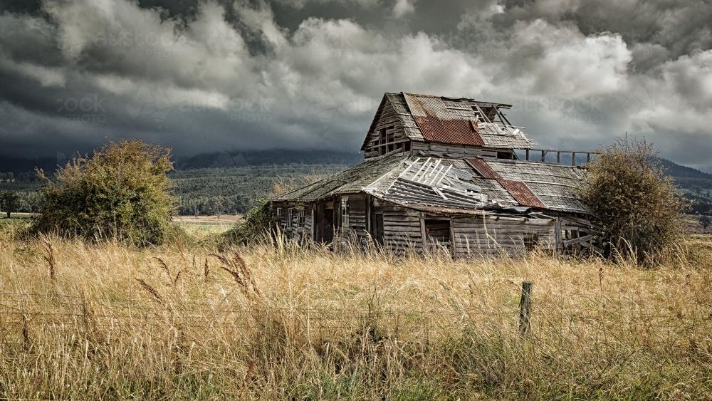 Derelict farmhouse in a paddock with dramatic sky in Tasmania - Australian Stock Image