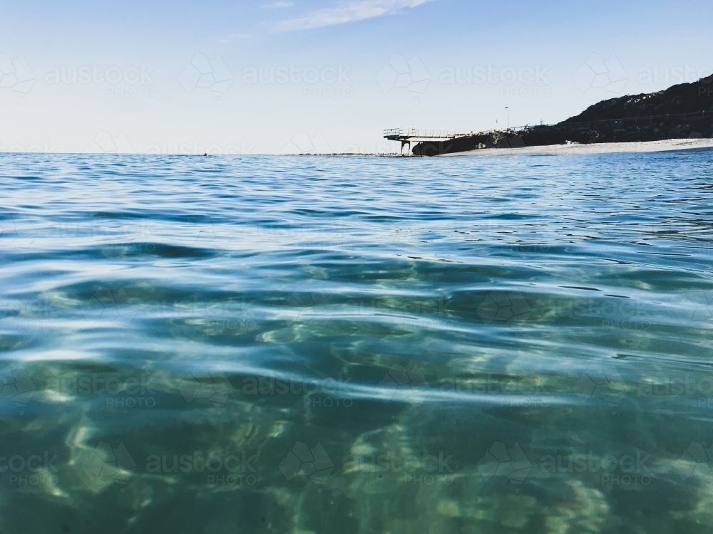 Deserted Ocean in foreground with jetty in background on calm clear sky day - Australian Stock Image