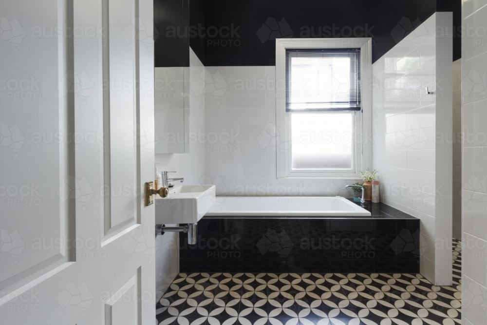 Designer bathroom renovation with monochrome moroccan floor tiles and black bath hob - Australian Stock Image
