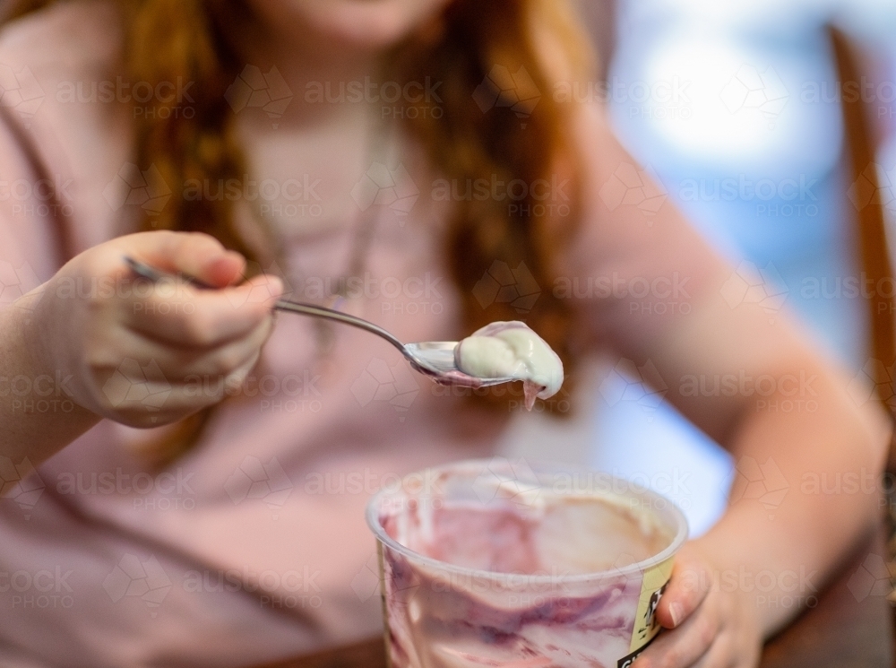 detail of child eating flavoured yoghurt from tub with a spoon - Australian Stock Image