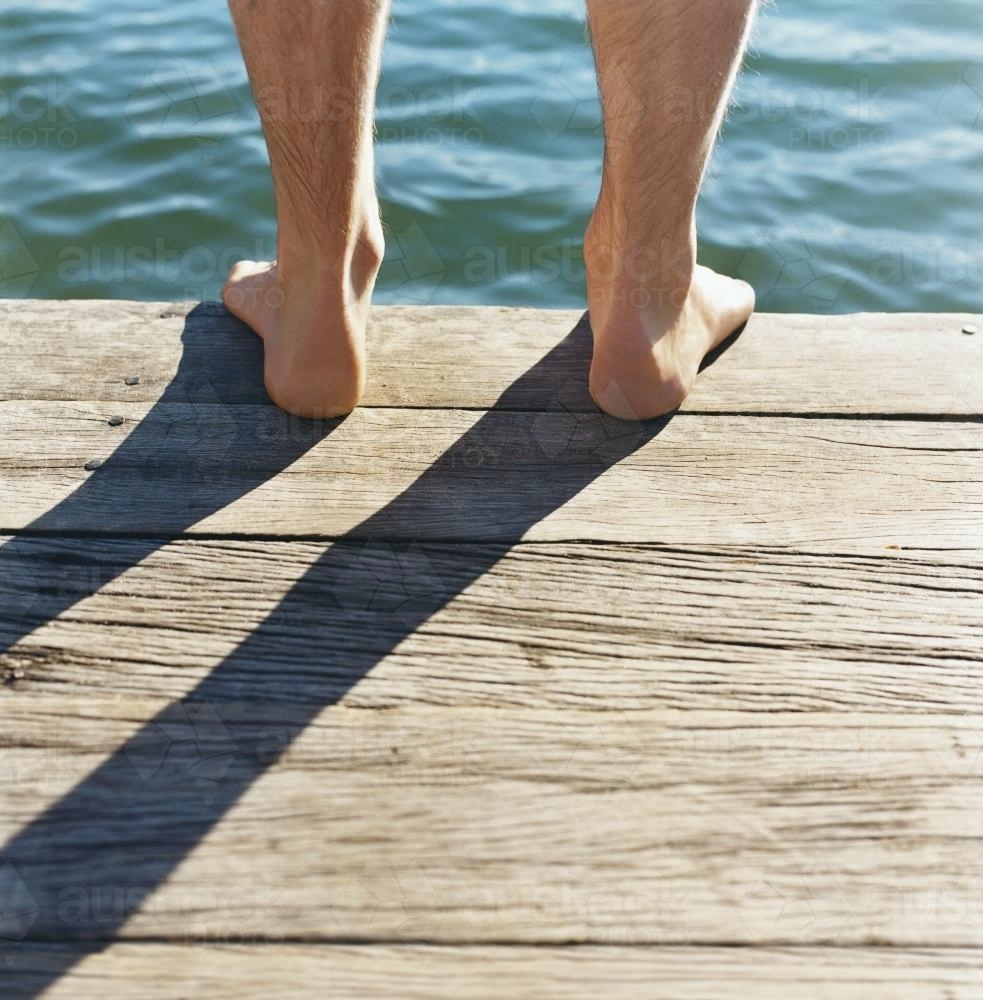 Detail of feet standing on wooden jetty with water in background - Australian Stock Image