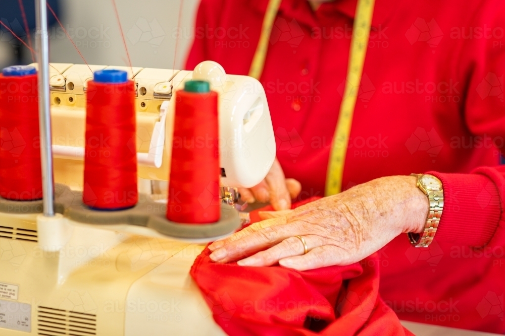 detail of lady sewing with red fabric on overlocker machine - Australian Stock Image