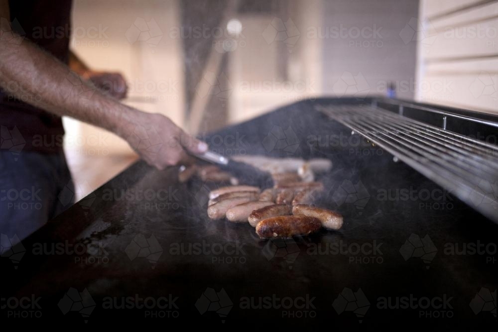 Detail of man cooking sausages on a barbeque - Australian Stock Image