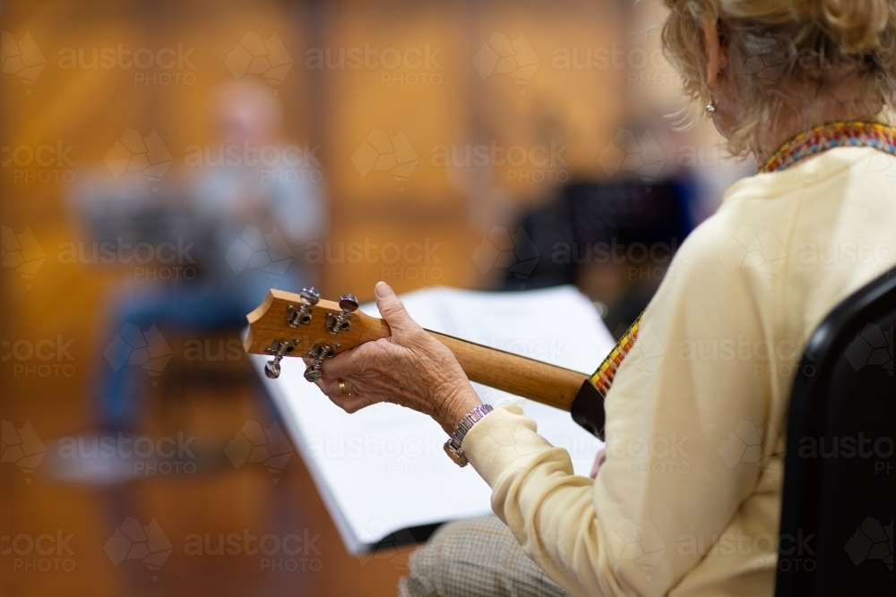detail of senior lady playing ukulele with blurred musician in background - Australian Stock Image