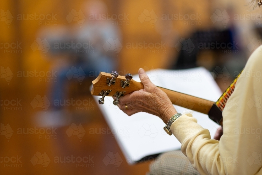 Image of detail of senior lady playing ukulele with blurred musician in